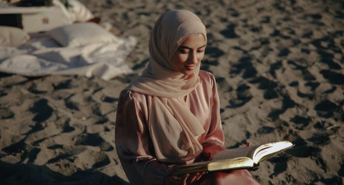 fair skinned woman in hijab reading on the beach.jpg.optimal