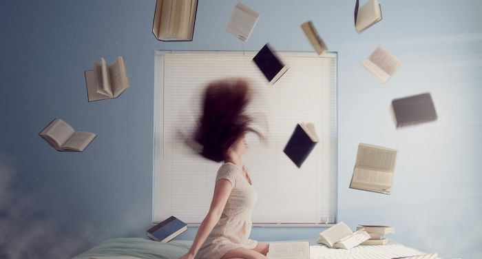 woman on bed with books flying through air.jpg.optimal