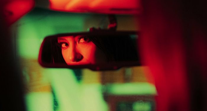 a lighter skinned woman looking in a rear view mirror in a car.jpg.optimal