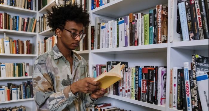 brown skinned Black man with kinky fro reading in a library .jpg.optimal