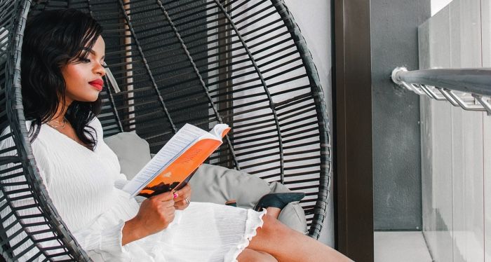 brown skinned Black woman with red lipstick reading in a wicker chair.jpg.optimal