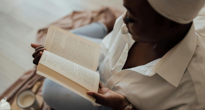 a dark brown skinned Black woman with a white head wrap sitting and reading a book.jpg.optimal